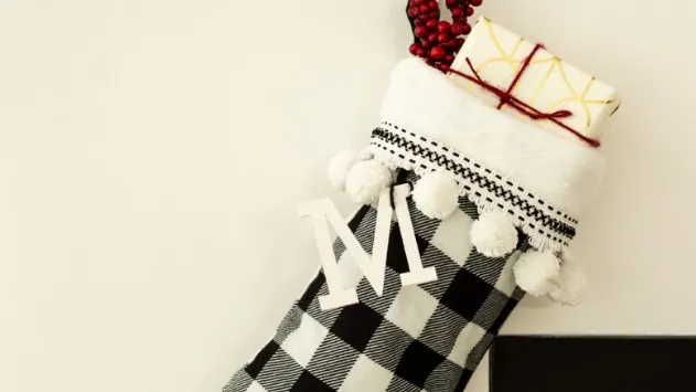 buffalo check Christmas stocking with a letter M monogram with a gift tucked inside and hanging from a fireplace mantel.
