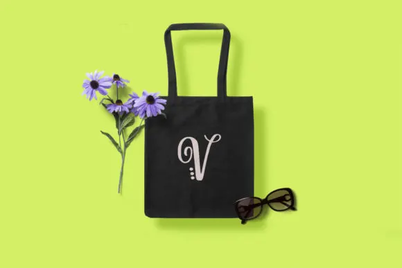 totebag with the letter V as a monogram next to flowers and sunglasses