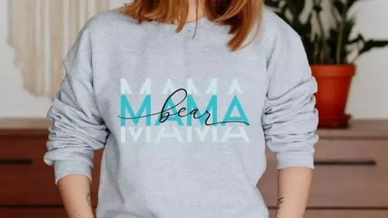 woman wearing a mother's day sweatshirt made with a mama bear font sublimation file. The sleeves of the sweatshirt have been pushed up to the elbows.