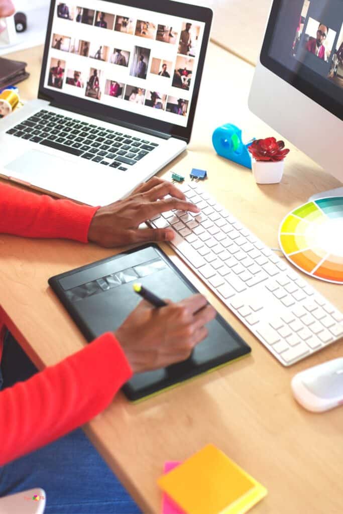 A person drawing svg files on a drawing tablet at desk with a laptop and a computer.