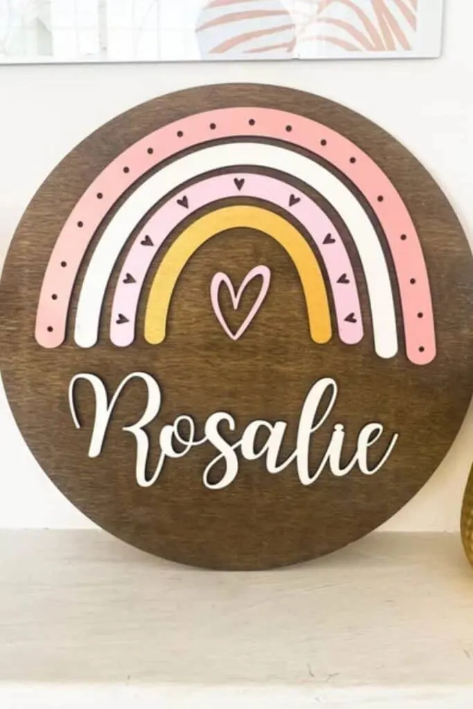 boho rainbow on a wooden circle with the name Rosalie beneath the rainbow.